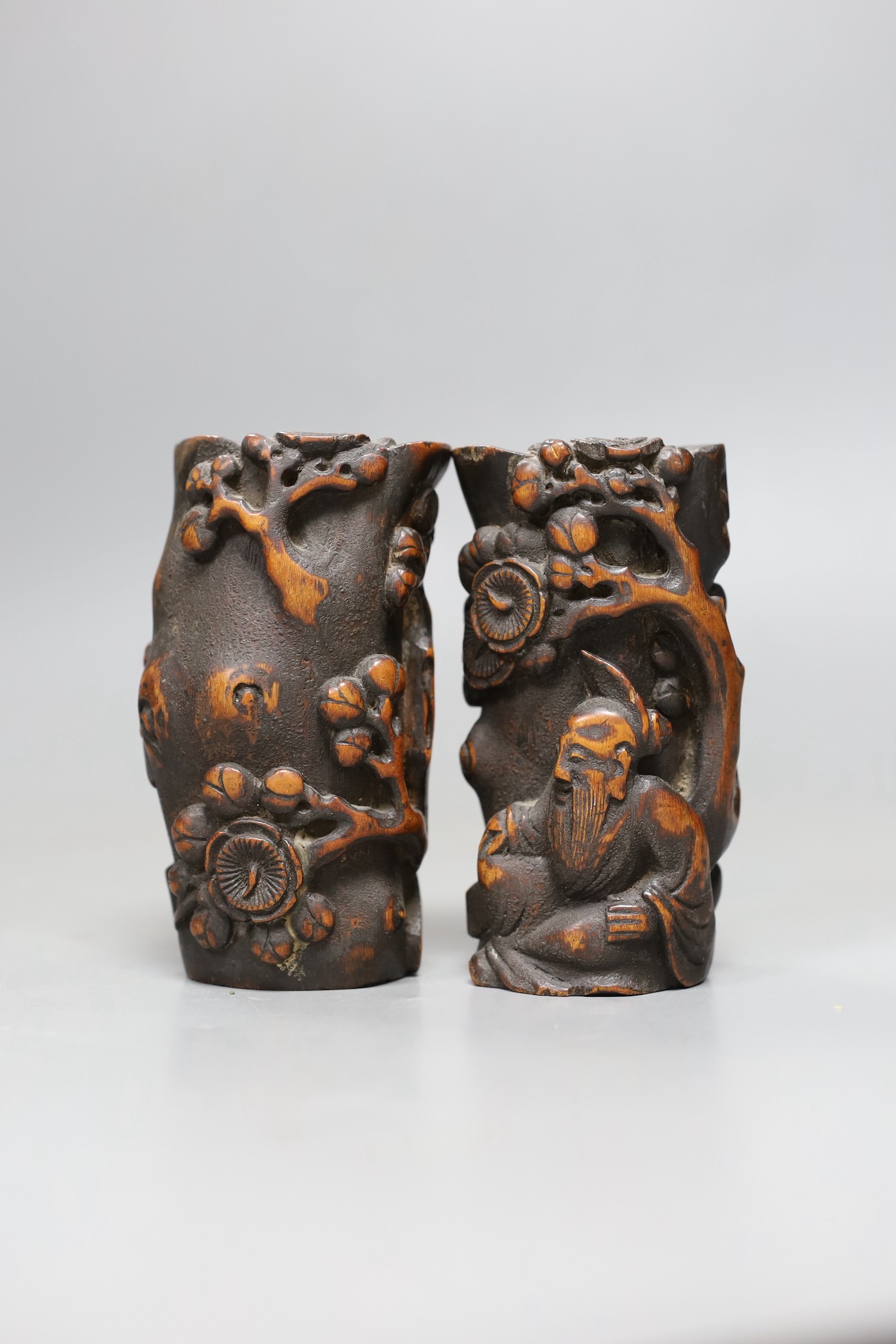 A pair of Chinese carved bamboo brush pots, late Qing dynasty, carved in high relief with a sage beneath a prunus tree, 11cms high